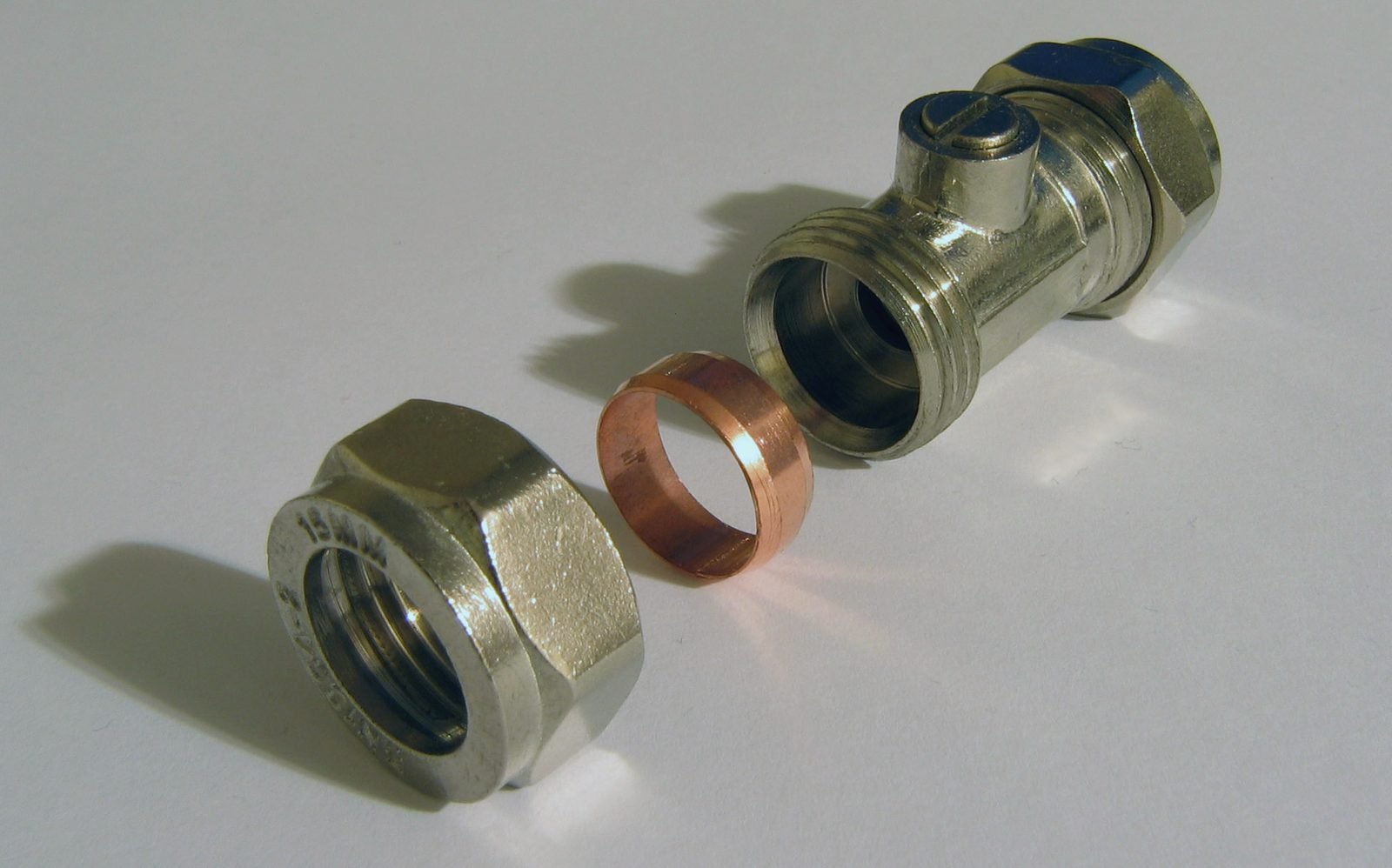 A brass compression fitting taken apart, with nut and copper olive