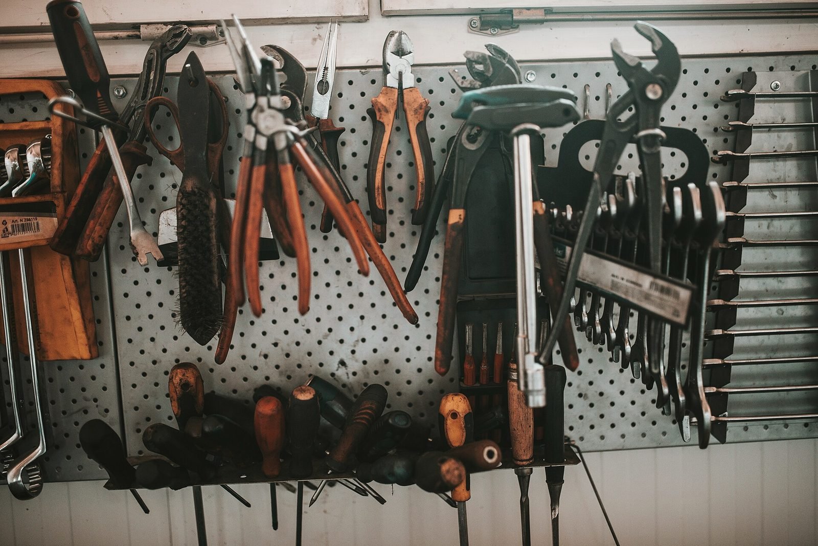 Pliers, snips and wrenches hanging on a black pegboard