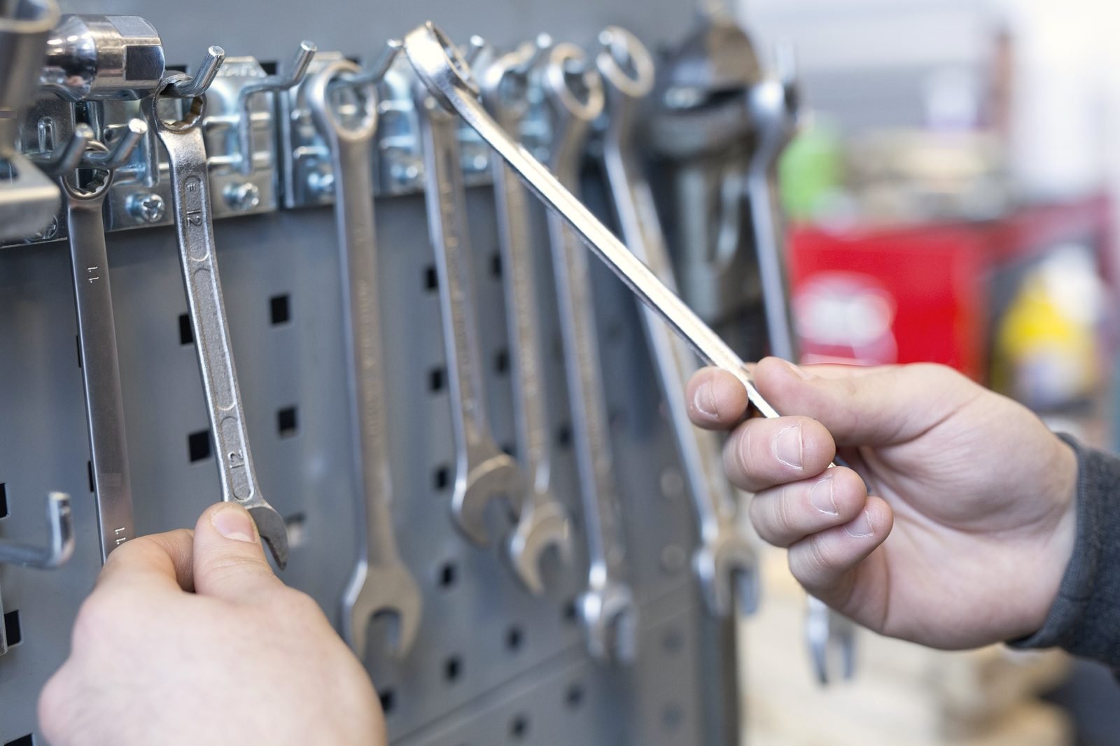 Two hands taking combination wrenches off a pegboard rack
